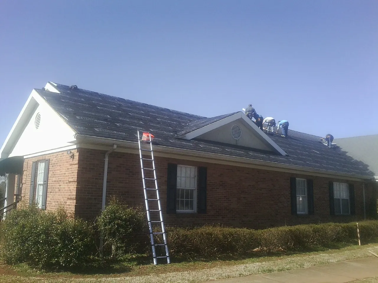 Crew tearing shingles off a brick ranch roof with a ladder set — Emergency Roof Repair work by our crew in Sedalia