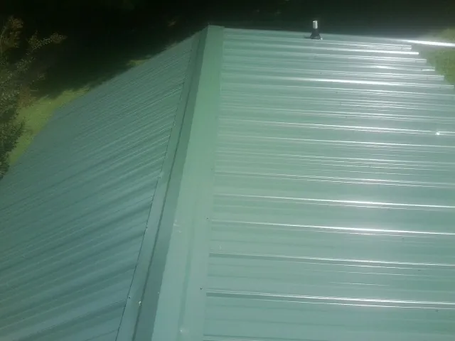 New green metal panels meeting at the ridge of a roof — Flat Roof Repair work by our crew in Sedalia
