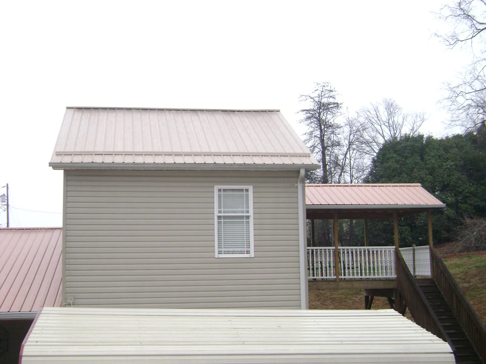 Tan metal roofs on a two story addition and attached porch, from a Roof Replacement job in Sedalia